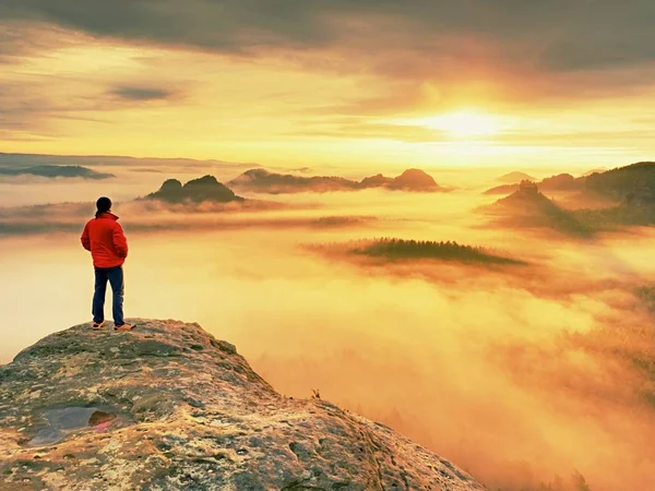 Турист в черном на скалистой вершине. Прекрасный рассвет в горах, тяжелый оранжевый туман в глубокой долине . — стоковое фото
