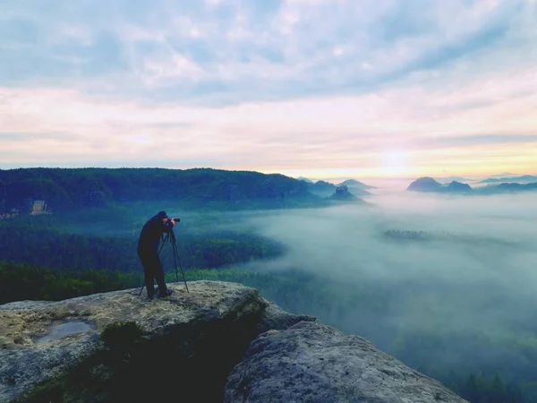 Professional on cliff. Nature photographer takes photos with mirror camera on peak of rock. Dreamy fog — Stock Photo, Image