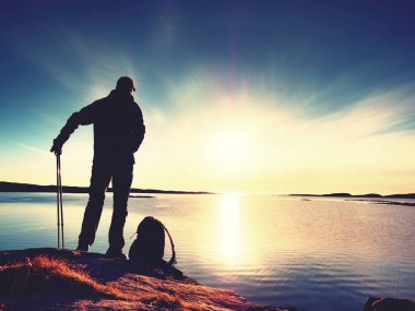 Uzun yürüyüşe çıkan kimse adam koyu spor giyim ve kayalık kıyılarında sportif sırt çantası ile. Mavi Gökyüzü bulutlu. Sihirli gün.