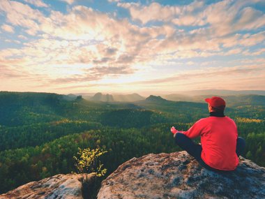Tek başına kayalıklarda oturan koyu kırmızı açık elbiseler uzun yürüyüşe çıkan kimse arka görünümü. Dağlar vadi, soğuk yukarıda kayalık tepe gizli yağmurlu bulutlar güneş keskin. 