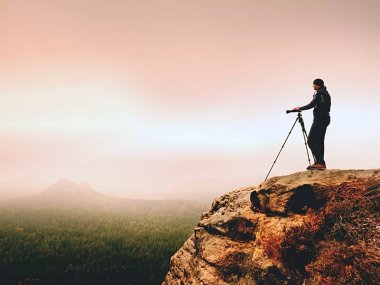 Sanat fotoğrafçısı yere tepe kaya üzerinde kamera ile fotoğraf çeker. Sisli manzara