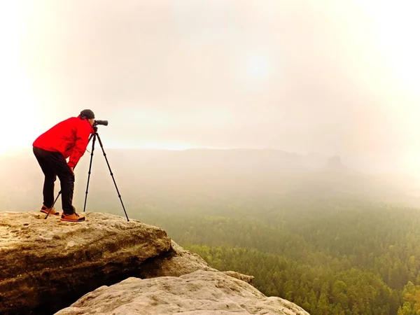 Fotógrafo mirando en el visor de la cámara digital dslr soporte en trípode. Artista fotografiando montaña y paisaje nublado — Foto de Stock