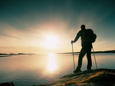 Uzun yürüyüşe çıkan kimse adam koyu spor giyim ve kayalık kıyılarında sportif sırt çantası ile. Mavi Gökyüzü bulutlu. Sihirli gün.