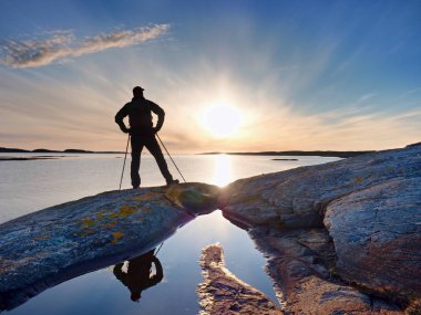 Uzun yürüyüşe çıkan kimse adam koyu spor giyim ve kayalık kıyılarında sportif sırt çantası ile. Mavi Gökyüzü bulutlu. Sihirli gün.