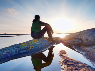 Taşlı sahil şeridi üzerinde oturan adam silüeti. Akşam güneşi Bay'e üzerinde görmek uzun yürüyüşe çıkan kimse