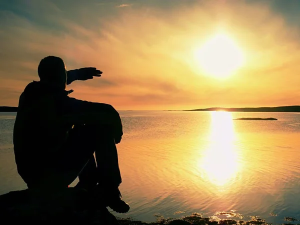 Esportista magro na costa rochosa sombreando olhos e olha para o sol de manhã acima do oceano liso. Maravilhoso dia — Fotografia de Stock