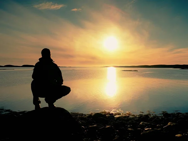 Man sit at evening sea. Hiker with backpack sit in squatting position  along beach. — Stock Photo, Image