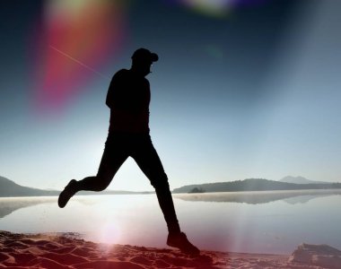 Kaçak ışık objektif. Adam siluet sabah güneş karşı sahilde egzersiz.