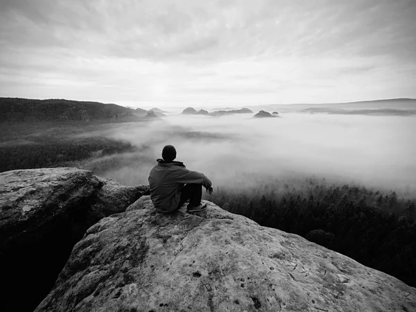 Wanderer auf dem felsigen Gipfel. herrlicher Tagesanbruch in den Bergen, dichter Nebel im tiefen Tal. . Schwarz-Weiß-Foto. — Stockfoto