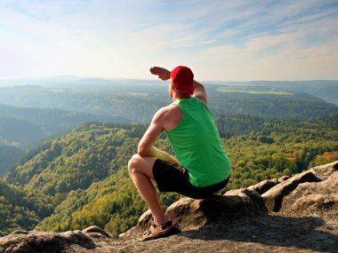 Yeşil singlet ve siyah şort ince gövde uzun yürüyüşe çıkan kimse kayanın üzerinde oturup, doğal sahne tadını çıkarın. Orman vadiye görüntülemek
