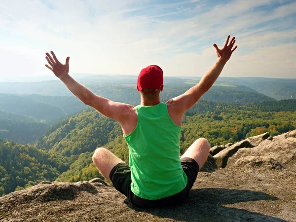Excursionista cuerpo delgado en soltera verde y pantalones cortos negros se sientan en una roca, disfrutar de paisajes naturales. Vista al valle del bosque — Foto de Stock