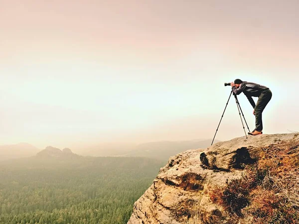 Fotógrafo profesional toma fotos de paisaje brumoso con cámara de espejo y trípode . — Foto de Stock