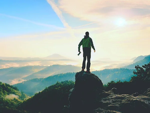 Фотограф с камерой в руках на вершине горы. Пеший турист взобрался на вершину скалы над туманной долиной — стоковое фото