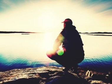 Adam akşam denizde otur. Uzun yürüyüşe çıkan kimse sırt çantası ile oturmak plaj boyunca çömelme pozisyonu.