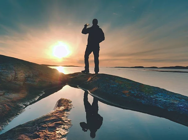 Silhouette posteriore dell'uomo viaggiatore che si fa selfie in mare. Turista con zaino in piedi su una roccia — Foto Stock