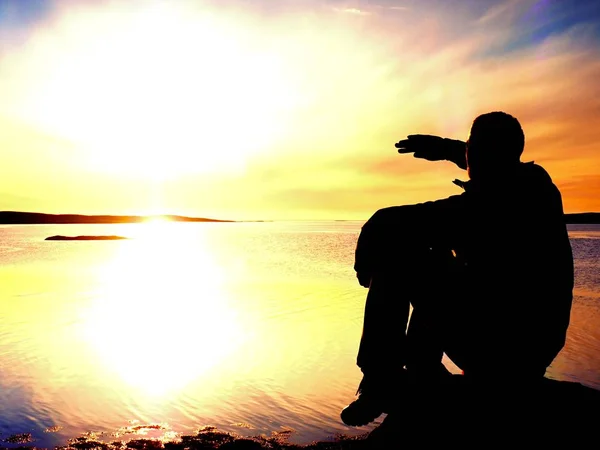 Slim sportsman on  rocky coast shadowing eyes and looks into mornning  sun above  smooth ocean. Marvelous  day — Stock Photo, Image