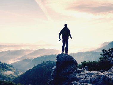 Fotoğrafçı dağın zirvesinde elinde kamerayla. Uzun yürüyüşe çıkan kimse rock sisli vadinin yukarıda zirvesine tırmandı