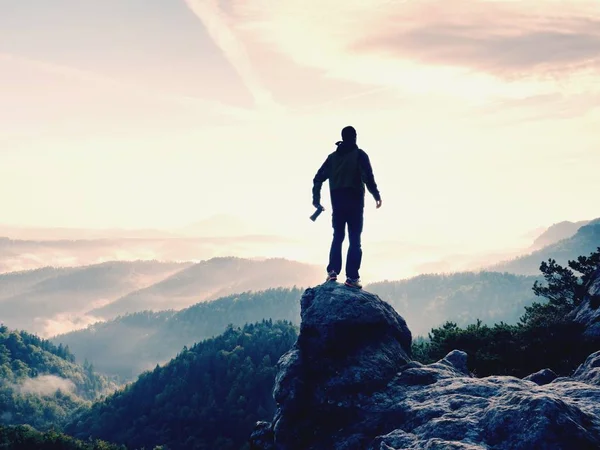 Photographer with camera in hands on top of mountain. Hiker climbed on peak of rock above foggy valley — Stock Photo, Image