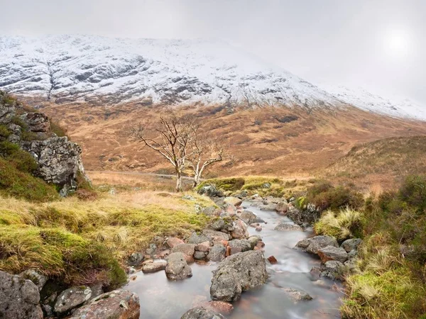 Dia nebuloso frio na primavera montanhas Higland na Escócia. Cone nevado de montanha em nuvens pesadas . — Fotografia de Stock