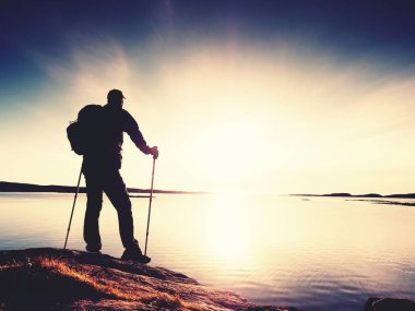 Uzun yürüyüşe çıkan kimse adam koyu spor giyim ve kayalık kıyılarında sportif sırt çantası ile. Mavi Gökyüzü bulutlu. Sihirli gün.