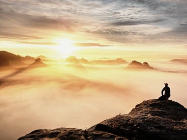 Siyah pantolon, ceket ve karanlık kap yetişkin turist oturup Cliff'in kenar ve puslu tepelik Vadisi'ne bakıyor