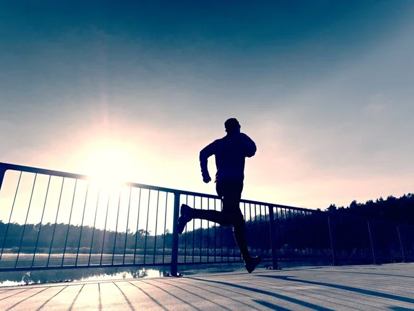 Morning runner in tall black leggings exercising  on bridge. Outdoor exercising on bridge