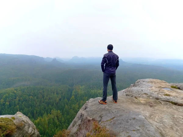 Nature hiker on sharp cliff roc watching over misty  valley to blurred horizon. Terrible rainy weathe