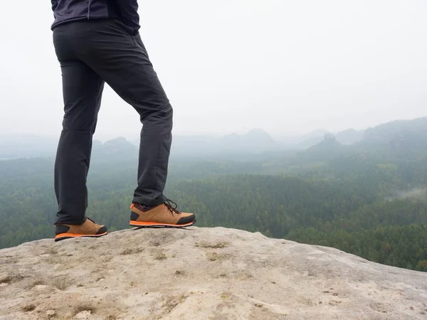 Manliga ben i mörk vandring byxor och trekking läderskor på toppen av rock ovanför misty valley. Disposition av hill — Stockfoto