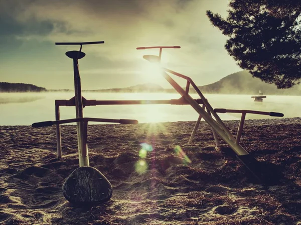 Övergivna baby swing på sandstranden vid sjön. Kall morgon efter säsong i holiday resort. — Stockfoto