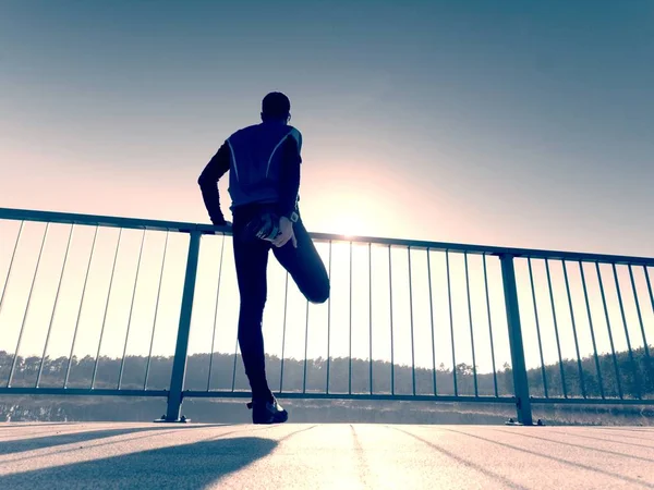 Corredor de la mañana en leggings negros altos hace que el cuerpo se estira en el camino del puente. Ejercicio al aire libre — Foto de Stock