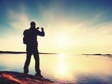 Adam silüeti kameralı cep telefonu anılarla elinde tutmak. Denizde muhteşem günbatımı
