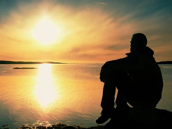 Jovem viajante ao pôr-do-sol. Turista sentado no penhasco acima do lago — Fotografia de Stock