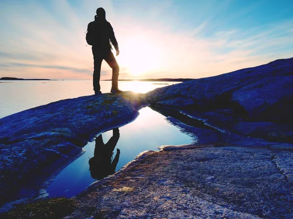 Joven hombre de pie con mochila. Caminante en la piedra en la orilla del mar en el cielo colorido del atardecer . —  Fotos de Stock