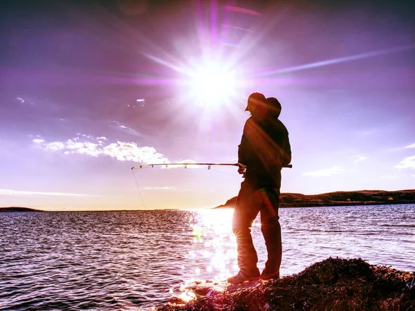 Hombre comprobar empujando cebo y lo lanza lejos en el mar. Pescador con caña — Foto de Stock