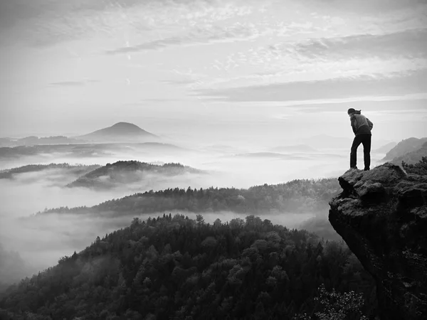 Mann bleibt bei Tagesanbruch auf felsigem Gipfel und wacht über neblige Landschaft. — Stockfoto