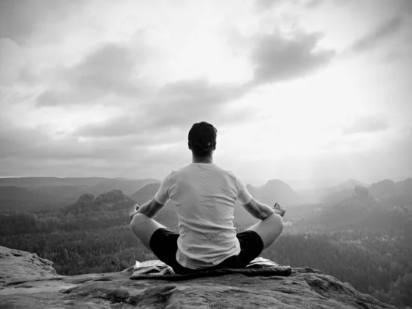 Solo seduto uomo praticare Yoga posa sulla vetta rocciosa. L'uomo al mattino nebbioso fa meditazione — Foto Stock