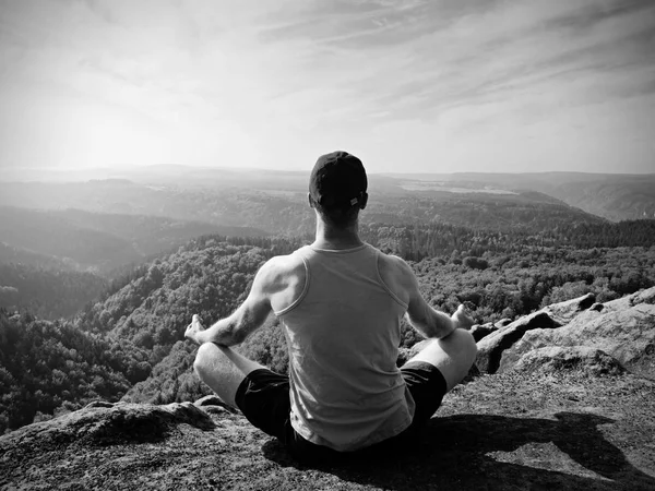 Slim corpo escursionista in single verde e pantaloncini neri sedersi su una roccia, godere di paesaggi naturali. Vista sulla valle del bosco — Foto Stock
