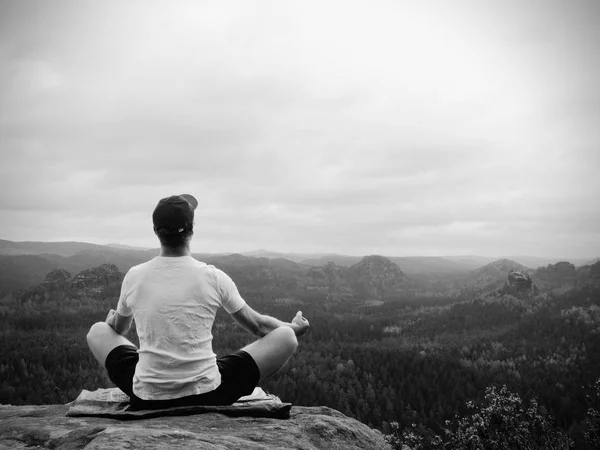 Solo seduto uomo praticare Yoga posa sulla vetta rocciosa. L'uomo al mattino nebbioso fa meditazione — Foto Stock