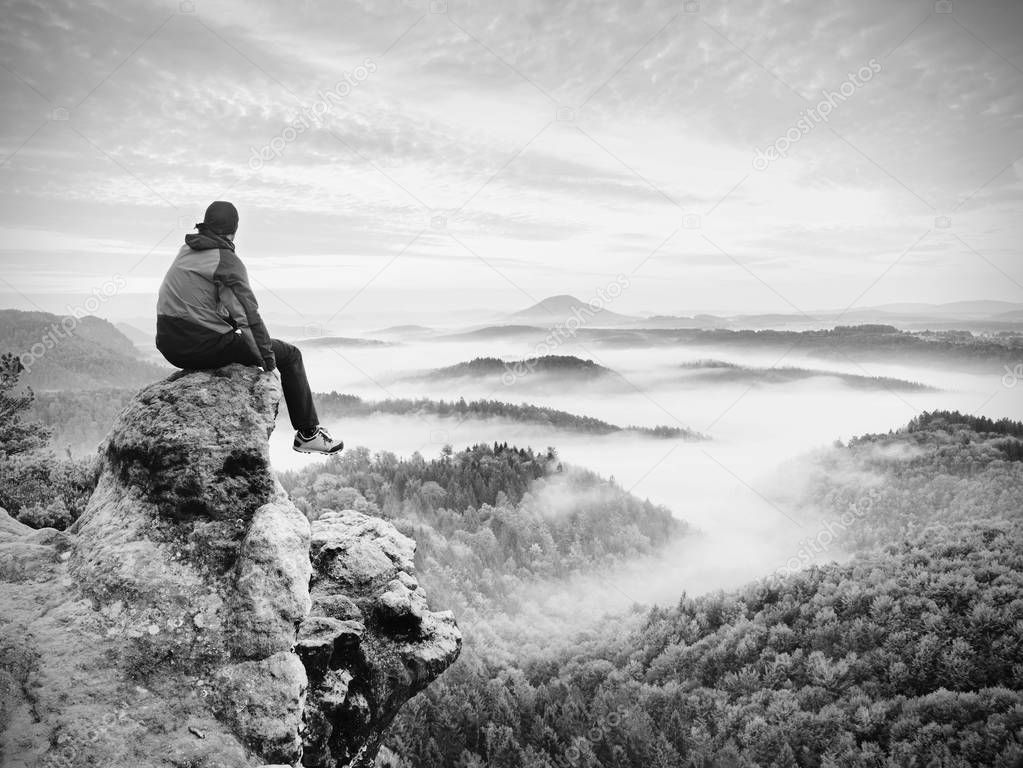 Hiker man take a rest on mountain peak. Man sit on sharp summit and enjoy spectacular view. 