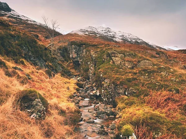 Avmarkera creek stream vatten strömmar över granitstenar. Snötäckta berg i tunga moln — Stockfoto