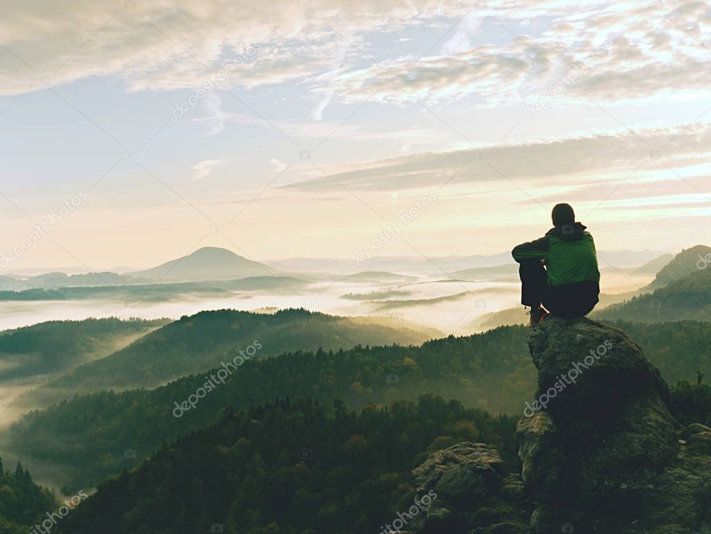 Hiker man take a rest on mountain peak. Man sit on sharp summit and enjoy spectacular view. 