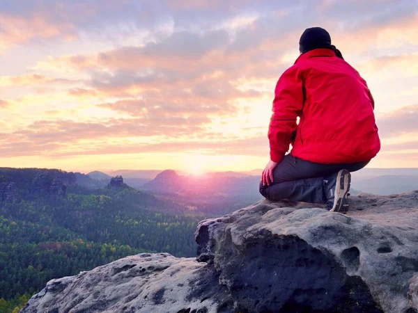 Сидящий турист на скале. Человек в красной черной теплой одежде сидит на скале и наслаждается далеким видом . — стоковое фото