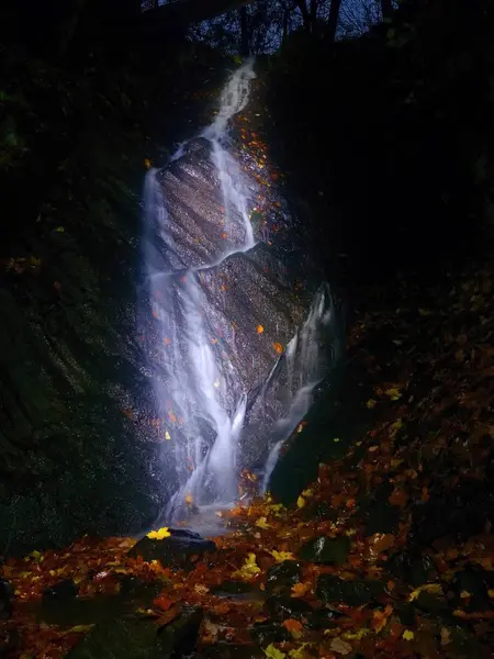 Cascada nocturna. Rocío de agua blanca en cascada en el arroyo, el agua espumosa está cayendo sobre la roca musgosa . — Foto de Stock