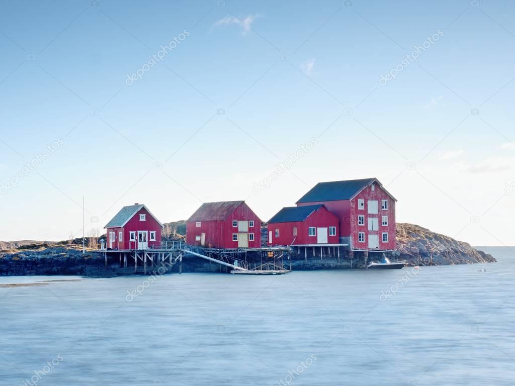Rural Norwegian landscape, traditional red and white wooden house on rocky island. Suny spring day with smooth water level in bay.