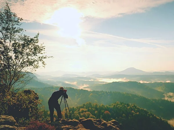 Nature photographer in the action.  Man silhouette above a misty clouds,