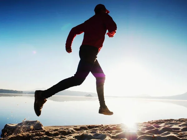 Hombre con gafas de sol, gorra de béisbol roja y ropa deportiva roja negra está corriendo y haciendo ejercicio en la playa . — Foto de Stock