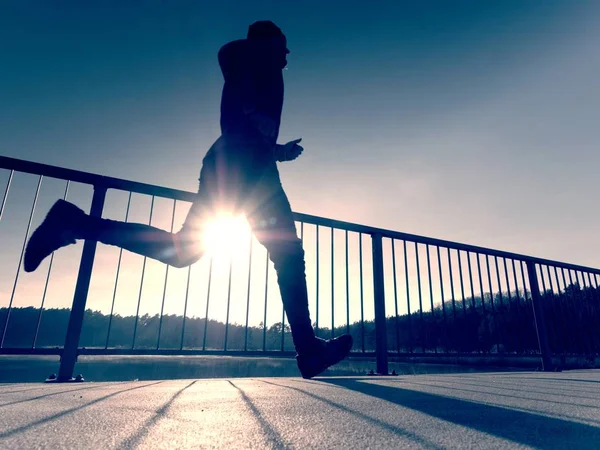 Visão traseira para corredor em camiseta azul e perneiras pretas correndo na ponte. Exercício ao ar livre Imagem De Stock