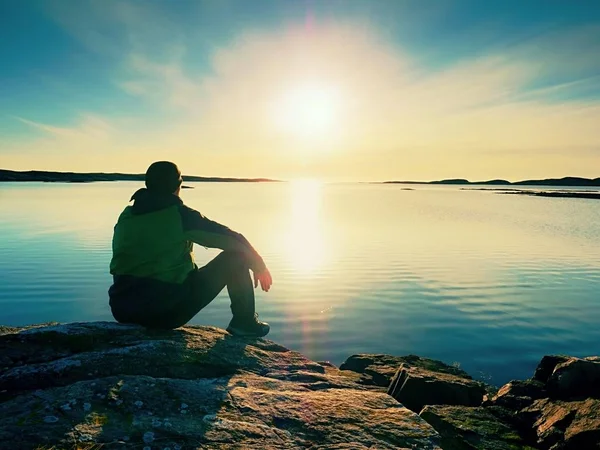 Einsamer Wanderer sitzt allein an der Küste und genießt den Sonnenuntergang. Blick über felsige Klippen zum Meer — Stockfoto