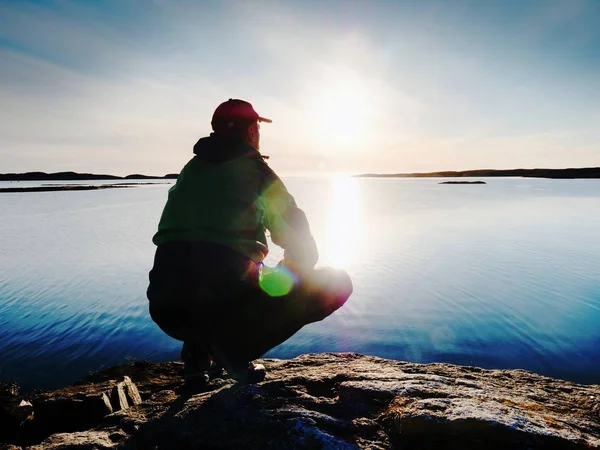 Junger Mann, der auf einem Felsen sitzt und einen wunderschönen Sonnenuntergang am Meer beobachtet. Wanderer genießen allein den Abend — Stockfoto