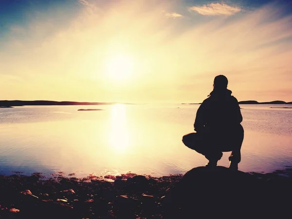 Giovane seduto su una roccia a guardare uno splendido tramonto sul mare. Escursionista da solo godersi la serata — Foto Stock